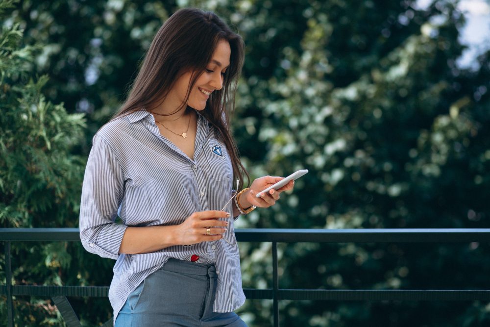 Mujer sonriente que usa su celular en una terraza rodeada de árboles